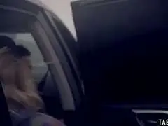 Blonde Anhalterin mit wehenden Haaren und tiefem Ausschnitt steht mit Rucksack am Straßenrand