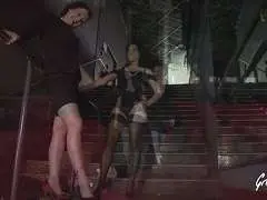 Dunkelhaarige Milf und schwarzhaarige Frau in engen Kleidern und High Heels stehen tagsüber vor modernem Gebäude