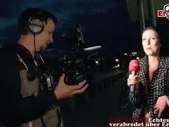 Schwarzhaarige Milf im Beanie interviewt abends einen Mann mit Mikrofon auf der Straße